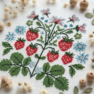 May include: A cross-stitch embroidery of a strawberry design. The piece features red strawberries, green leaves, blue flowers, and red and blue floral accents on a white background. The artwork is square and detailed.