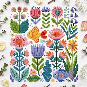 Può includere: Un motivo a punto croce su tessuto bianco che presenta una varietà di fiori colorati nelle tonalità del rosa, arancione, viola e giallo, intervallati da fogliame verde e due pesci stilizzati, uno arancione e uno blu, disposti in una griglia.
