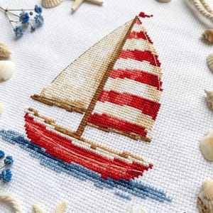 May include: Cross-stitch sailboat with red and white striped sail, beige sail, and red hull. The boat is on blue water. The background is white with seashells, starfish, and blue flowers.