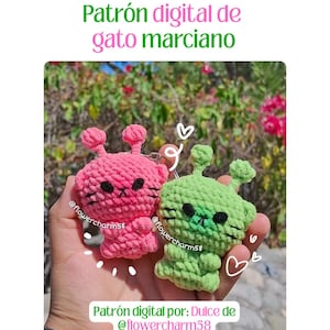 Puede incluir: Se muestran dos llaveros de gato alienígena de ganchillo, uno rosa y otro verde. El llavero rosa tiene ojos negros y una nariz negra. El llavero verde también tiene ojos negros y una nariz negra. El texto "Patrón digital de gato marciano" está en la parte superior.