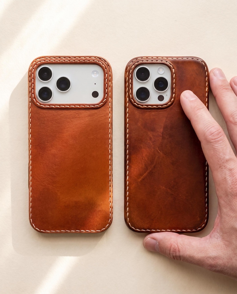 May include: Two rectangular phone cases crafted from smooth, tan-colored leather with visible light-colored stitching along the edges. Each case features a cutout for the camera module, exposing the white back of the phone and the lens array.