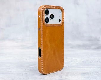 May include: A tan leather phone case with white stitching and a white interior. The case has a rectangular shape with rounded corners and a camera cutout. The case has a stitched border and a small metal accent.