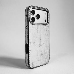May include: A black and white phone case with a distressed, weathered texture and visible stitching along the edges. The case features a cutout for the camera module, which contains three circular lenses, and a small star symbol on the side.