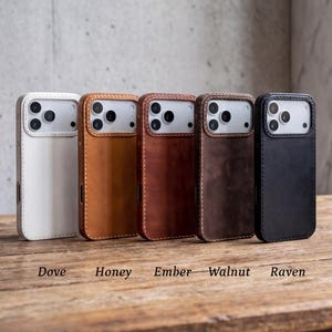 May include: Five smartphone cases arranged in a row, featuring colors labeled as Dove, Honey, Ember, Walnut, and Raven. Each case has a rectangular cutout for the camera module and visible stitching along the edges of the protective cover.