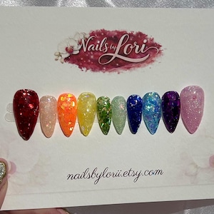 Könnte beinhalten: Ein Satz regenbogenfarbener, glitzerbedeckter Kunstnägel. Die Nägel sind in einer Reihe angeordnet, jede in einer anderen Farbe des Regenbogens. Die Karte trägt den Text "Nails by Lori" und die Website-Adresse "nailsbylorii.etsy.com".