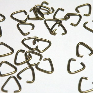 May include: A pile of small, gold-colored metal triangle jump rings. The rings are about 1/2 inch in diameter.
