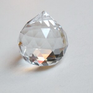May include: A clear crystal ball with a faceted design. The ball is round and has a pointed top.