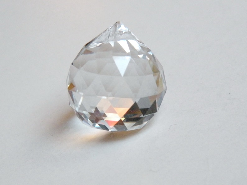 May include: A clear crystal ball with a faceted design. The ball is round and has a pointed top.