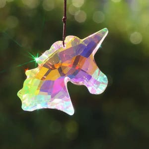 May include: A crystal unicorn suncatcher with iridescent rainbow colors hanging from a brown string.