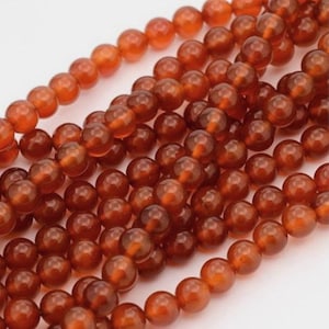 May include: Close-up of strands of round, translucent, amber-colored beads. The beads have a polished, glossy finish and are strung together, creating a textured surface. The beads are a warm, earthy tone, ideal for jewelry making or crafting.