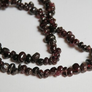 May include: A strand of dark red gemstone beads, likely garnet, strung on a clear thread. The beads are irregularly shaped and have a natural, rough texture.