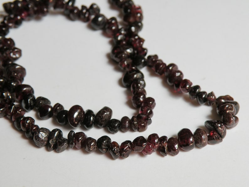 May include: A strand of dark red gemstone beads, likely garnet, strung on a clear thread. The beads are irregularly shaped and have a natural, rough texture.
