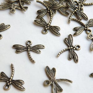 May include: A group of antique bronze dragonfly charms with intricate details. The charms have a textured surface and are perfect for jewelry making or crafting.