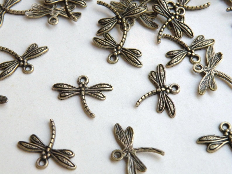 May include: A group of antique bronze dragonfly charms with intricate details. The charms have a textured surface and are perfect for jewelry making or crafting.
