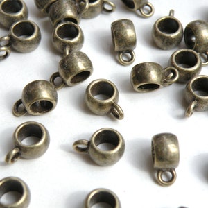 May include: A group of antique gold-toned metal bead caps with a loop on top. The bead caps are scattered on a white surface.