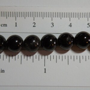 May include: A strand of black gemstone beads, each bead is approximately 1.2 cm in diameter. The beads are lined up next to a ruler, showing the size of the beads.