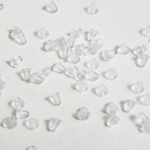 May include: A large quantity of clear plastic earring backs scattered on a white surface.