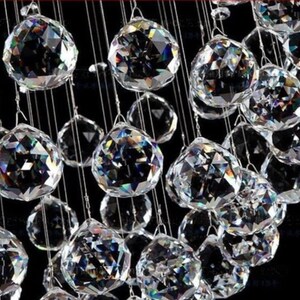 May include: A close-up of a crystal chandelier with many clear, faceted crystal balls hanging from a metal frame. The crystals reflect light and create a sparkling effect.
