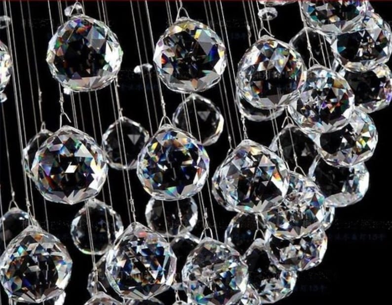 May include: A close-up of a crystal chandelier with many clear, faceted crystal balls hanging from a metal frame. The crystals reflect light and create a sparkling effect.