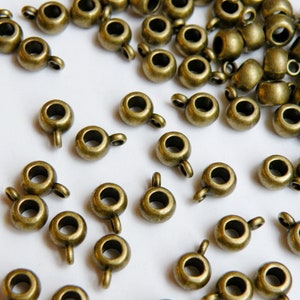 May include: A large quantity of antique gold-toned metal bead caps with a loop on each side. The bead caps are scattered on a white surface.