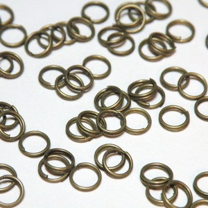 May include: A large quantity of small, gold-toned metal jump rings. The rings are all the same size and are arranged in a random pattern on a white surface.