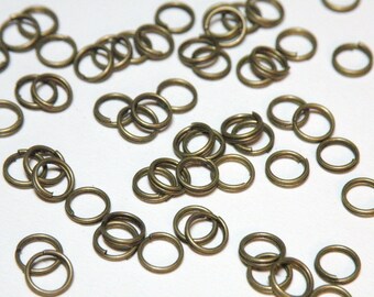 以下が含まれることがあります： たくさんの小さな金色の金属製のジャンプリング。リングはすべて同じサイズで、白い表面にランダムに配置されています。