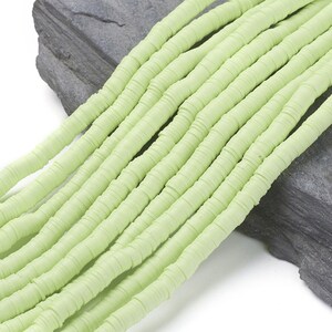 Könnte beinhalten: Eine Strähne aus hellgrünen Polymer-Tonperlen. Die Perlen sind flach und rund und zu einer langen Reihe aufgereiht. Die Perlen sind versetzt angeordnet, so dass sie sich leicht überlappen.