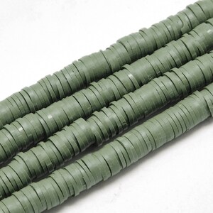 Könnte beinhalten: Eine Strähne grüner Polymer-Tonperlen, jede Perle ist ein Stapel dünner, flacher Scheiben. Die Perlen sind in einer Reihe angeordnet, wobei sich die Enden der Strähne überlappen.