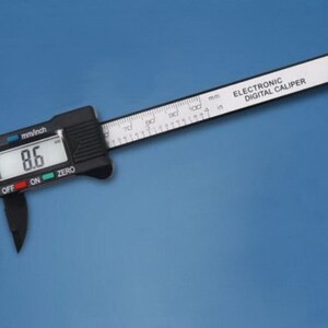 May include: A black electronic digital caliper with a white display showing 8.6 mm/inch. The caliper has a black and white ruler with markings in millimeters and inches. The text "ELECTRONIC DIGITAL CALIPER" is printed on the ruler.