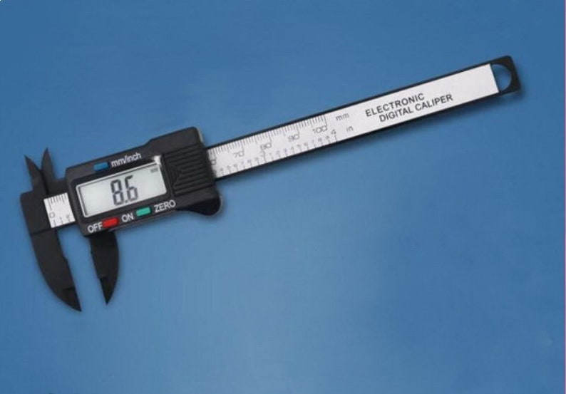 May include: A black electronic digital caliper with a white display showing 8.6 mm/inch. The caliper has a black and white ruler with markings in millimeters and inches. The text "ELECTRONIC DIGITAL CALIPER" is printed on the ruler.