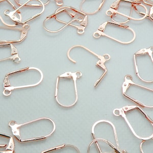 May include: A close-up of a group of rose gold earring hooks. The hooks are made of metal and have a simple, elegant design.