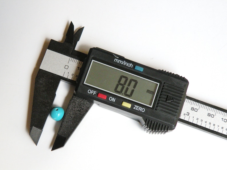 May include: A black digital caliper measuring a turquoise bead. The caliper reads 8.0 mm.