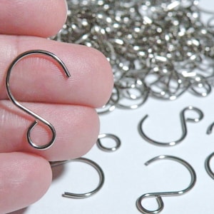 May include: A close-up of a silver S-shaped hook, held in a hand. The hook is a common type of hardware used for hanging items. There are many other silver S-shaped hooks in the background.