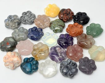 Puede incluir: Una colección de piedras preciosas pulidas talladas con forma de huellas de animales. Las piedras presentan diversos colores y texturas, incluyendo minerales en blanco translúcido, azul intenso, gris moteado, rosa, morado, verde, naranja y negro.