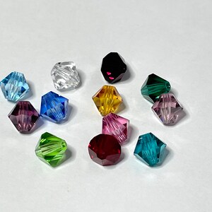 May include: Assortment of 12 faceted glass beads in various colors, including clear, light blue, dark blue, purple, green, yellow, and red. The beads are all the same size and shape, and they have a shiny, reflective finish.