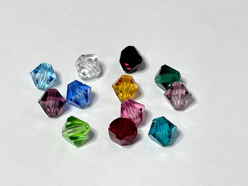 May include: Assortment of 12 faceted glass beads in various colors, including clear, light blue, dark blue, purple, green, yellow, and red. The beads are all the same size and shape, and they have a shiny, reflective finish.