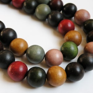 May include: A close-up of a strand of wooden beads in various colors, including red, black, green, and brown. The beads are round and have a smooth finish. The beads are likely used for jewelry making or other crafts.