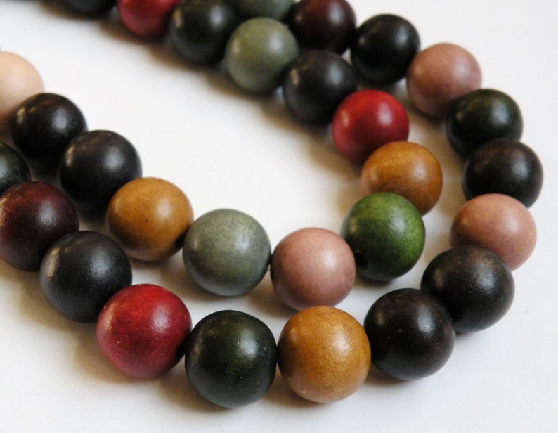 May include: A close-up of a strand of wooden beads in various colors, including red, black, green, and brown. The beads are round and have a smooth finish. The beads are likely used for jewelry making or other crafts.