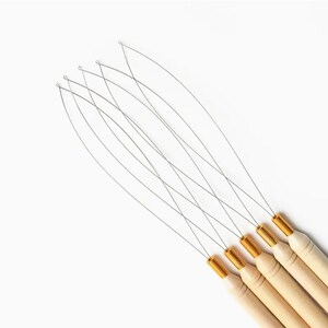 May include: A set of six hair extension tools. Each tool has a thin, silver wire loop attached to a wooden handle with a gold-colored metal ferrule. The tools are arranged diagonally against a white background.