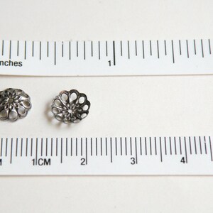 Op de afbeelding: Twee zilveren metalen kralencaps met een decoratief, opengewerkt ontwerp. De caps zijn ongeveer 2,5 cm in diameter.