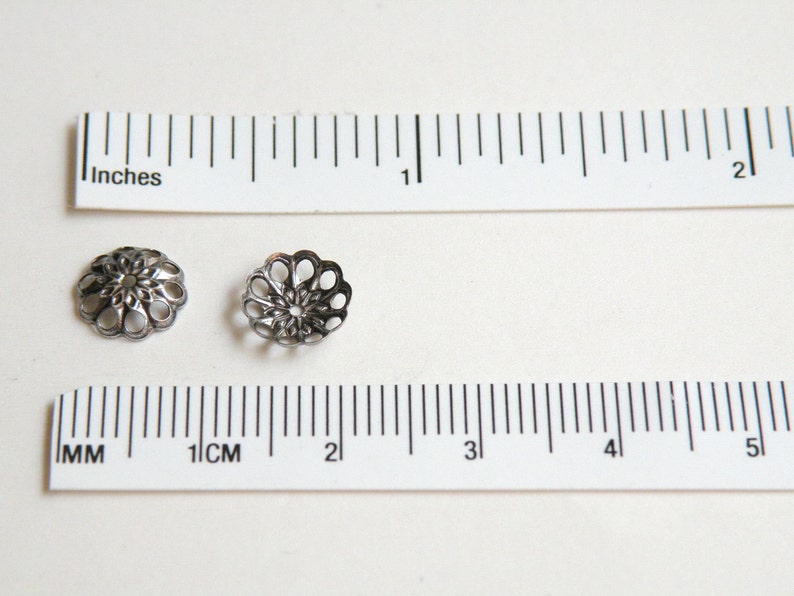 Op de afbeelding: Twee zilveren metalen kralencaps met een decoratief, opengewerkt ontwerp. De caps zijn ongeveer 2,5 cm in diameter.