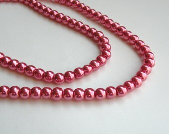 May include: A strand of pink faux pearl beads. The beads are strung on a clear thread and are arranged in a double strand.