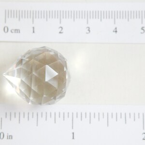May include: A clear glass crystal prism with a teardrop shape and faceted sides. The prism is approximately 1 inch in diameter.