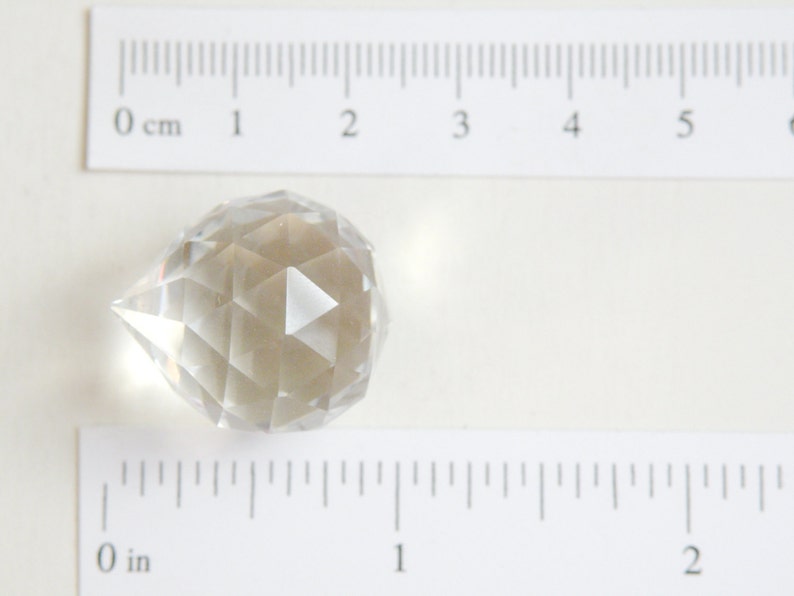 May include: A clear glass crystal prism with a teardrop shape and faceted sides. The prism is approximately 1 inch in diameter.