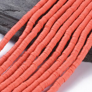 Könnte beinhalten: Eine Strähne aus leuchtend orangefarbenen Polymer-Tonperlen. Die Perlen sind flach und rund, mit einer leicht strukturierten Oberfläche. Sie sind auf einem durchsichtigen Faden aufgefädelt.