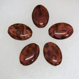 May include: Five oval-shaped beads with a marbled pattern in shades of brown and pink. The beads have a glossy finish.