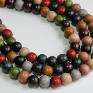 May include: Close-up of three strands of wooden beads in various colors, including red, black, green, brown, and gray. The beads are round and appear to be strung together, creating a necklace or craft supply.