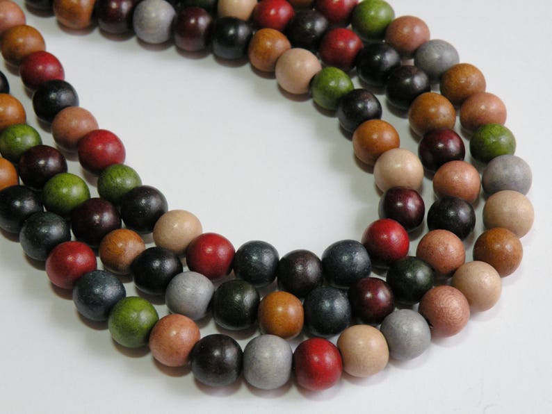 May include: Close-up of three strands of wooden beads in various colors, including red, black, green, brown, and gray. The beads are round and appear to be strung together, creating a necklace or craft supply.