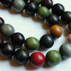 May include: A strand of wooden beads in various colors, including dark red, black, green, and tan. The beads are round and appear to be made of wood. The beads are strung together, creating a necklace or bracelet.