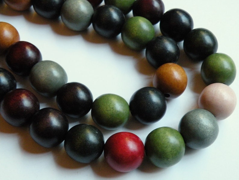 May include: A strand of wooden beads in various colors, including dark red, black, green, and tan. The beads are round and appear to be made of wood. The beads are strung together, creating a necklace or bracelet.